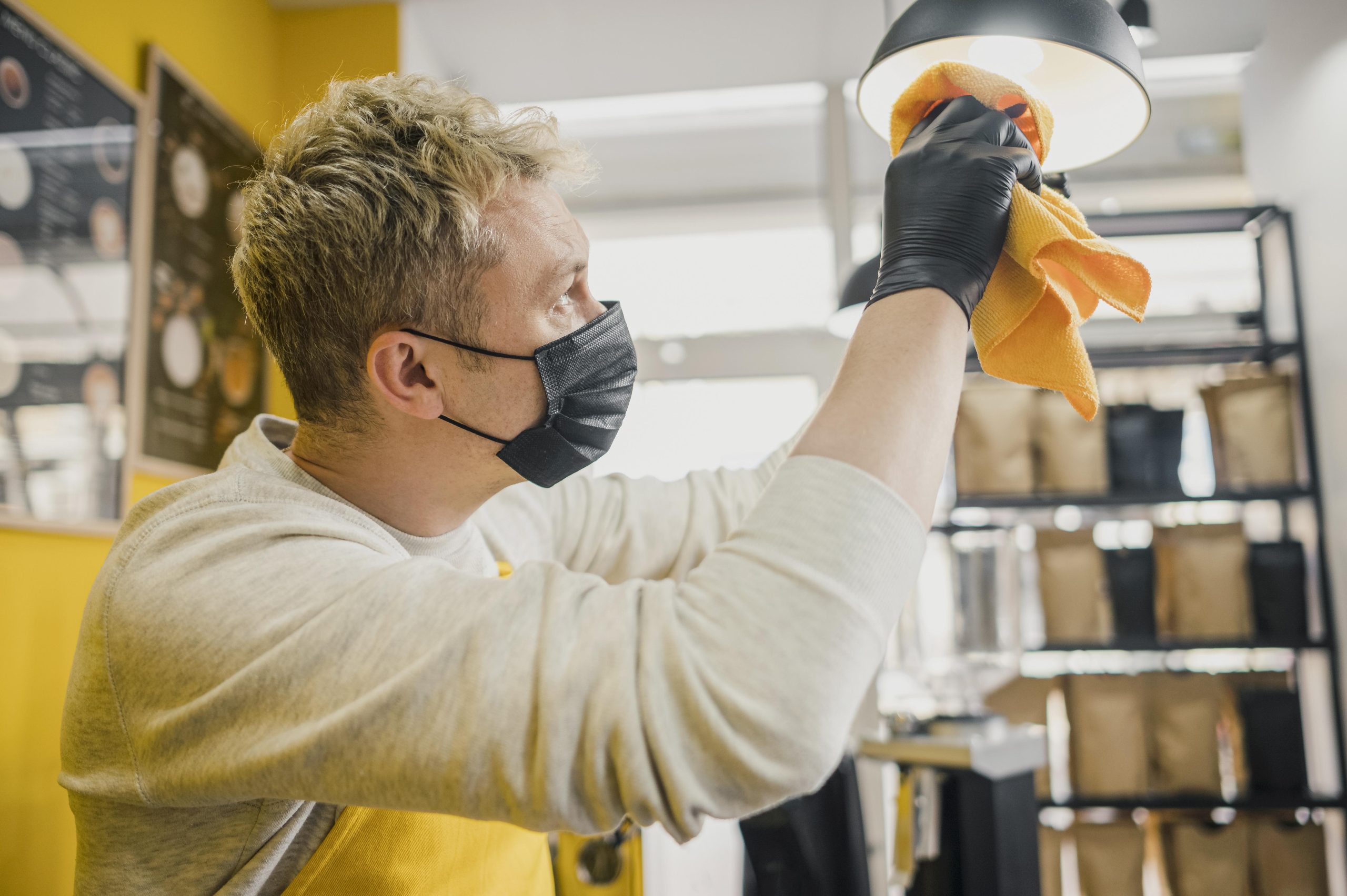 side-view-male-barista-with-medical-mask-cleaning-lamps-coffee-shop